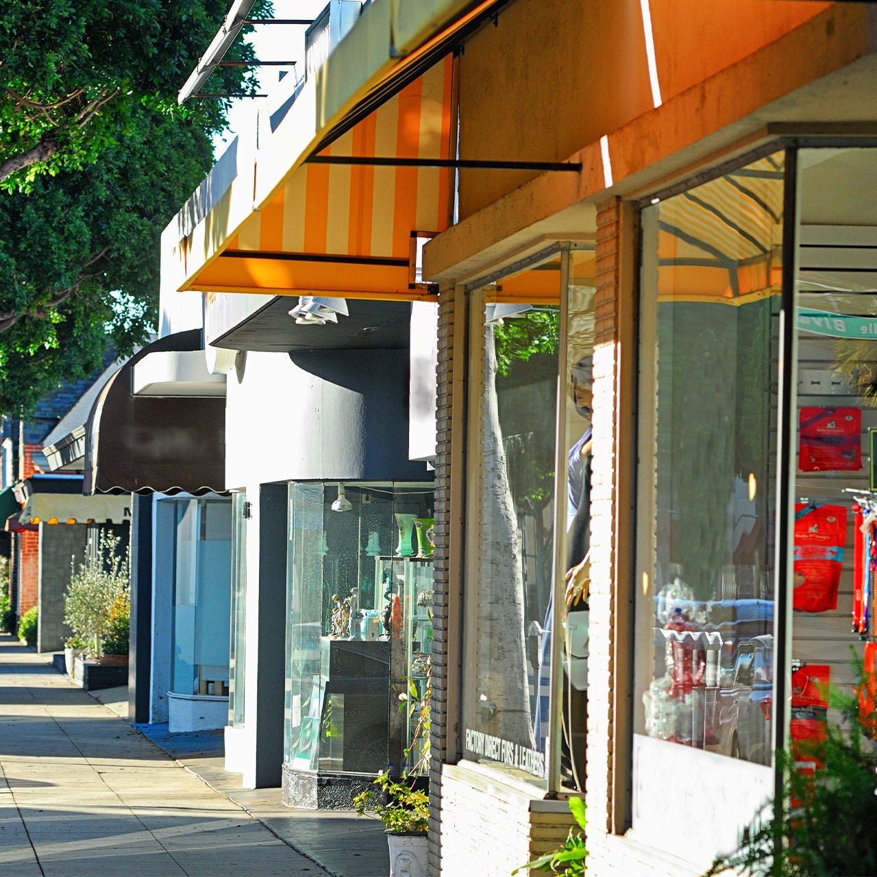 A row of small storefronts lines a bright urban sidewalk on a sunny day