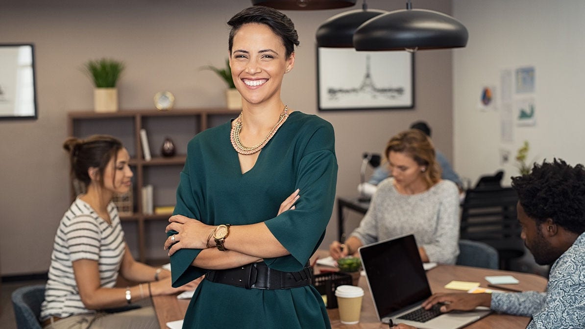 A woman smiling standing in front of a table with coworkers working behind her