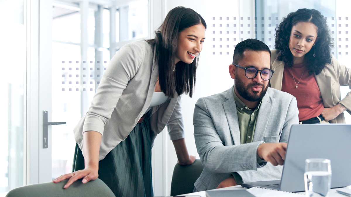 Three professionals are gathered around a laptop in a bright, modern office environment