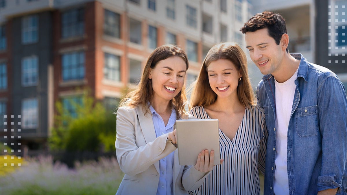 Three young adults stand together outdoors looking at a digital tablet