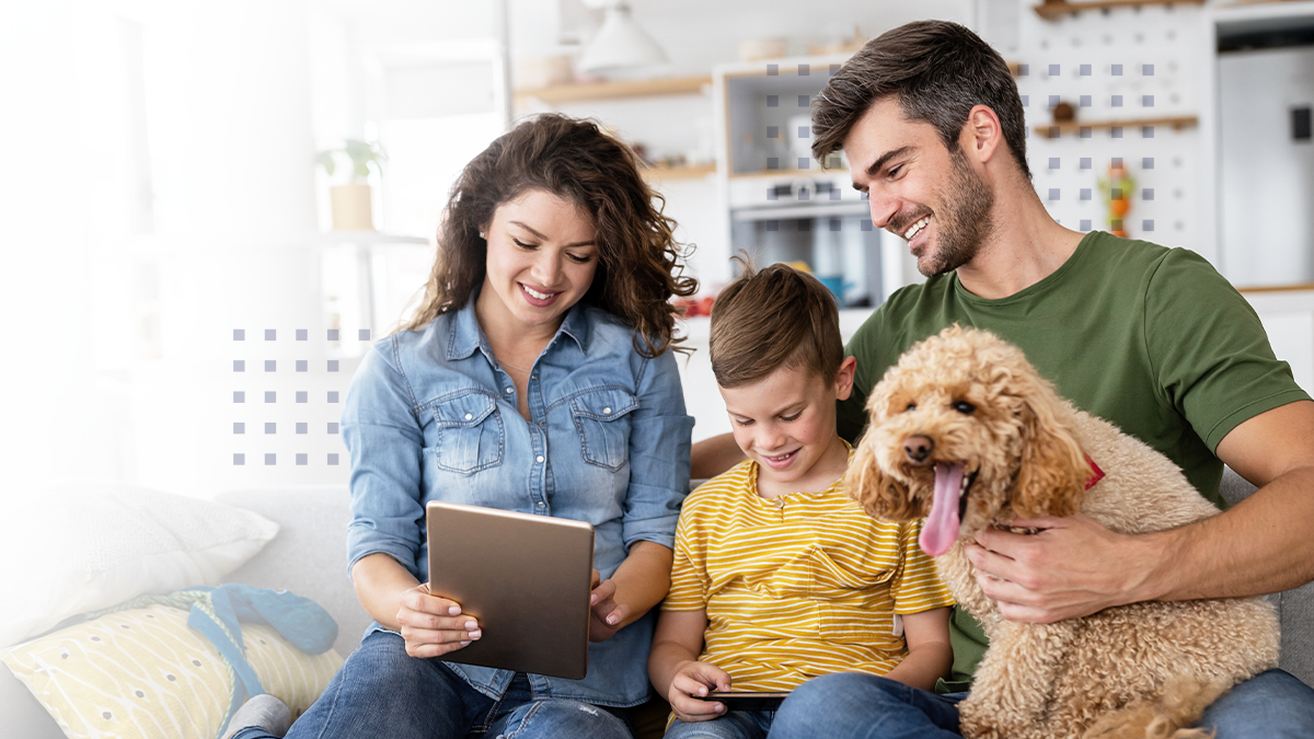 A smiling family sitting on a couch with a dog while using their electronic devices