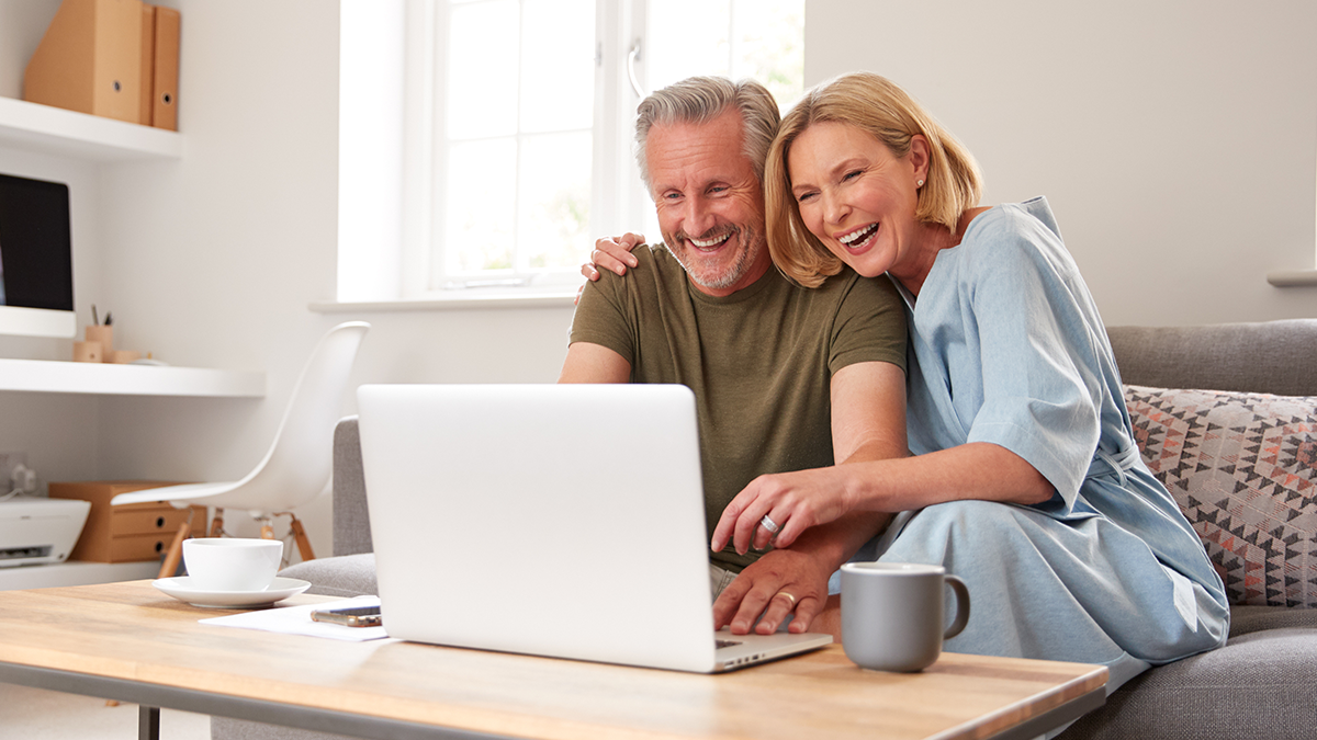 Smiling elderly couple looking at laptop screen using wifi at home