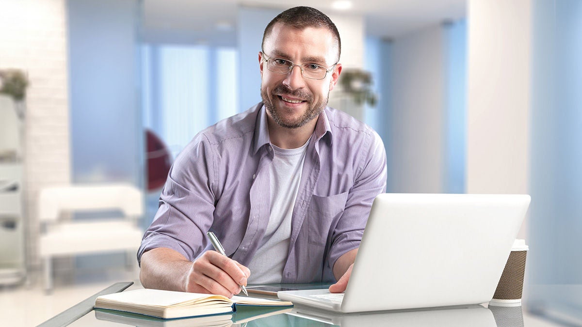 Man smiling and learning with laptop and notebook
