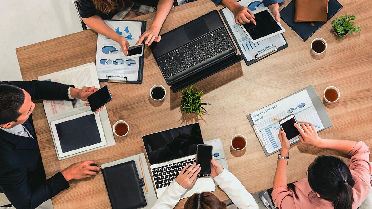 Employees using electronic devices at a table with an overlay of abstract marketing icons