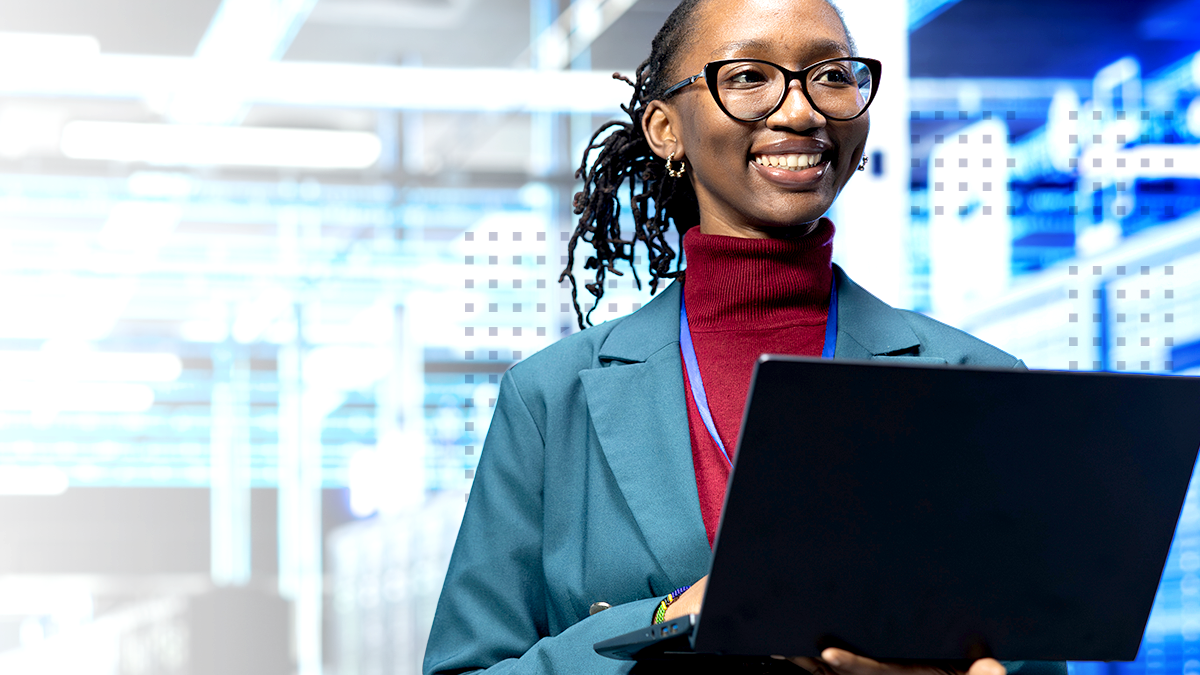 A smiling professional holds an open laptop while standing in a bright, modern technology environment