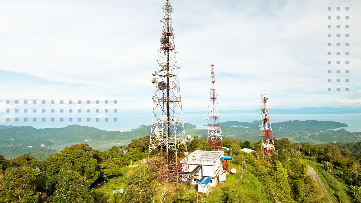 An aerial view of a grassy rural area with three cell towers and a building