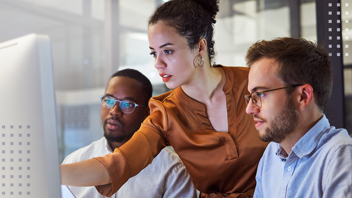 Three coworkers gather around a large desktop monitor in a modern office working together, solving problems, and involved in collaborative decision making