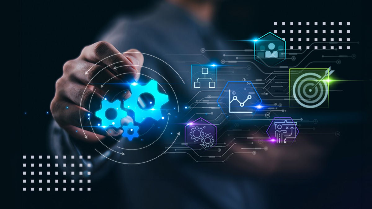 A person in a dark setting reaches forward to touch a glowing blue gear icon, symbolizing automation and process optimization. Around the hand, colorful holographic interface elements depict data analytics, home or cloud connectivity, and a target icon representing goals or strategy. The background is blurred and dark, emphasizing the bright neon graphics and futuristic technology theme. The overall composition suggests digital transformation, innovation, and modern business solutions.