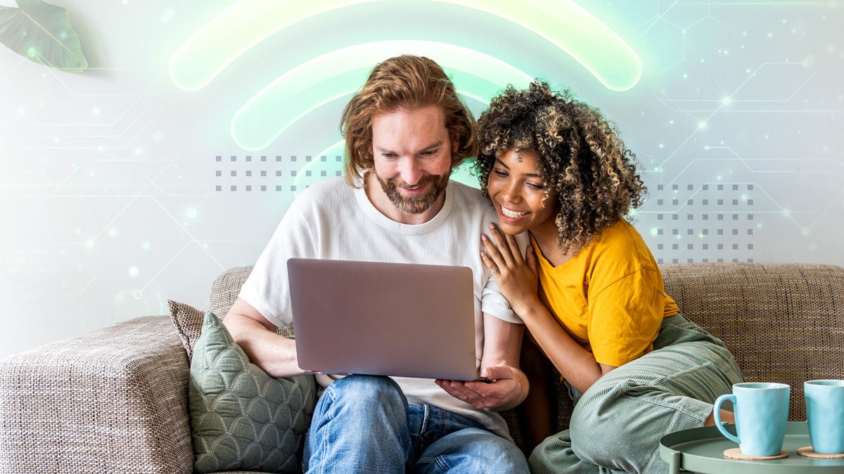 A smiling couple sits closely together on a living room sofa, looking at a laptop screen. A glowing wireless signal graphic arches above them, suggesting strong home Wi-Fi connectivity. Soft pastel colors and digital light effects create a modern, tech-friendly atmosphere. A coffee table with cups and a cozy pillow add to the relaxed, domestic setting.