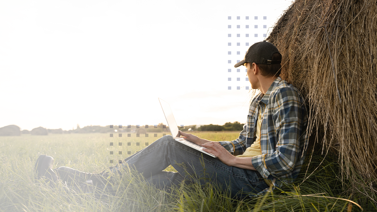 A man sitting in a rural field while using a laptop connected to a broadband infrastructure