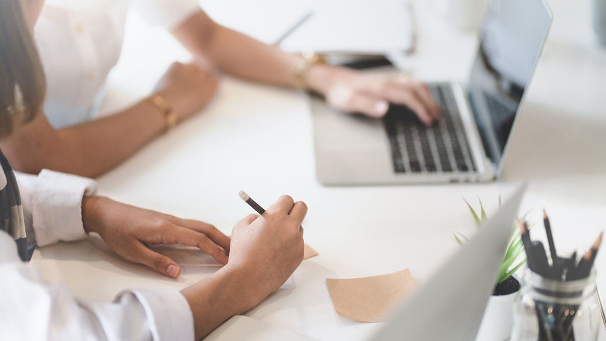 Two females working at a desk taking notes and using a laptop