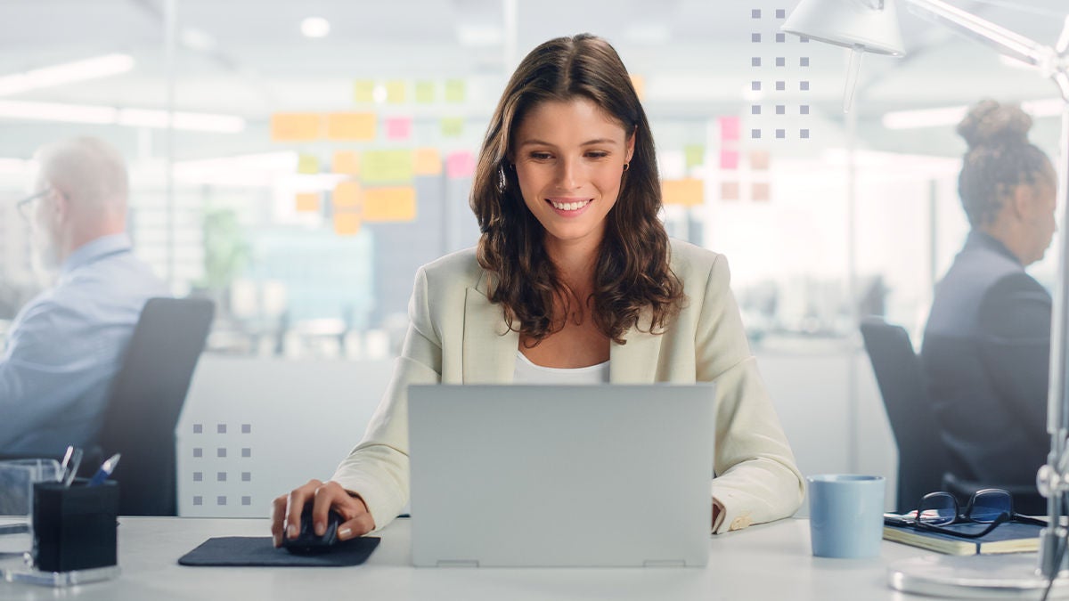 A young professional woman sits at a desk using a laptop in a modern office