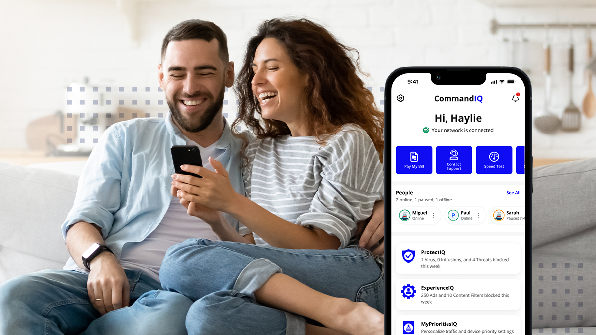 Smiling overjoyed wife and husband looking at phone screen, sitting on sofa in modern living room